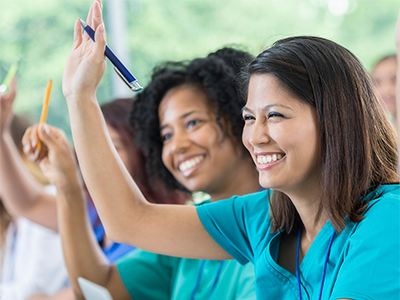 Couple of female medical students smiling and raising their hands in a classroom. 