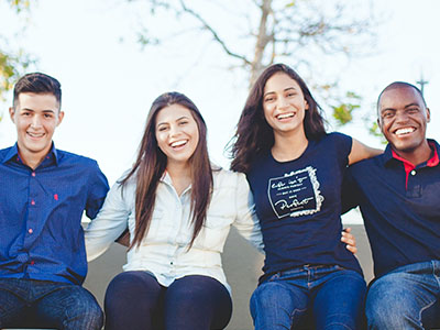 Diverse group of young adults sitting outside and smiling with arms around each other.